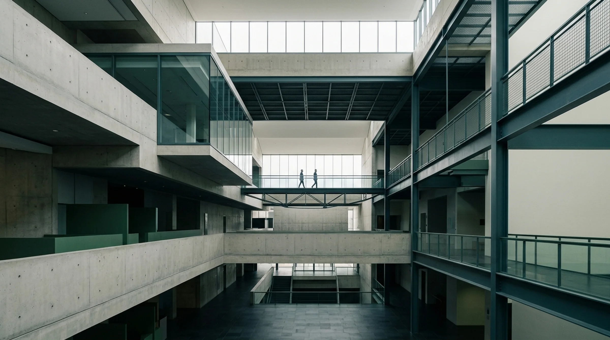 Expansive architectural interior of a contemporary civic building with layered concrete cantilevers, steel geometry and two distant figures on an elevated walkway